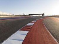 an empty track with red and blue stripes near a highway with a bridge in the background