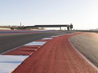 an empty track with red and blue stripes near a highway with a bridge in the background