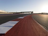 an empty track with red and blue stripes near a highway with a bridge in the background