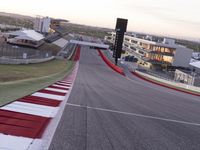 an empty race track with a building in the background and a red car sitting on the side of the track