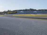 an empty race track with some grass and trees on the hillside behind it and a building in the distance