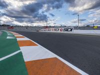 the race track is empty during a cloudy day with an orange and white paint line