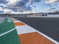 the race track is empty during a cloudy day with an orange and white paint line