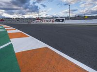 the race track is empty during a cloudy day with an orange and white paint line