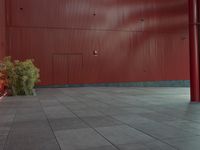 an empty red structure with large doors and windows in the corner of it that is surrounded by tall buildings