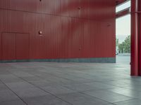 an empty red structure with large doors and windows in the corner of it that is surrounded by tall buildings