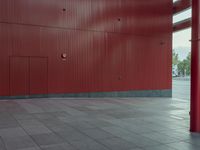 an empty red structure with large doors and windows in the corner of it that is surrounded by tall buildings