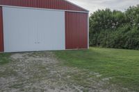 an empty red and white building is near a grassy field and two trees in the distance