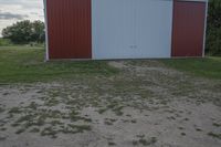 an empty red and white building is near a grassy field and two trees in the distance