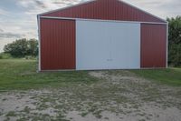 an empty red and white building is near a grassy field and two trees in the distance