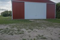 an empty red and white building is near a grassy field and two trees in the distance