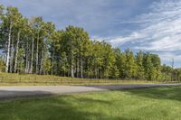 an empty road and grassy field with trees in the background that appear to be in an area outside a fenced area