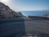 an empty road running along a cliff overlooking the water and ocean with rocks in the foreground