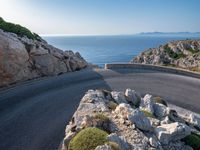 an empty road running along a cliff overlooking the water and ocean with rocks in the foreground