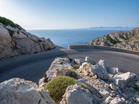 an empty road running along a cliff overlooking the water and ocean with rocks in the foreground