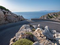 an empty road running along a cliff overlooking the water and ocean with rocks in the foreground