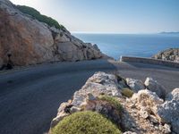 an empty road running along a cliff overlooking the water and ocean with rocks in the foreground