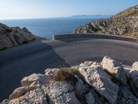 an empty road running along a cliff overlooking the water and ocean with rocks in the foreground