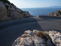 an empty road running along a cliff overlooking the water and ocean with rocks in the foreground