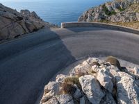 an empty road running along a cliff overlooking the water and ocean with rocks in the foreground