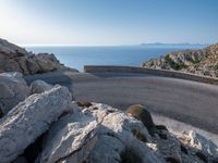 an empty road running along a cliff overlooking the water and ocean with rocks in the foreground