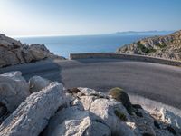 an empty road running along a cliff overlooking the water and ocean with rocks in the foreground