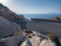 an empty road running along a cliff overlooking the water and ocean with rocks in the foreground