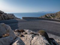 an empty road running along a cliff overlooking the water and ocean with rocks in the foreground