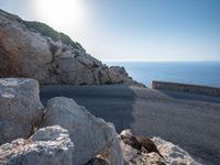 an empty road running along a cliff overlooking the water and ocean with rocks in the foreground