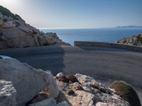 an empty road running along a cliff overlooking the water and ocean with rocks in the foreground