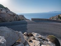 an empty road running along a cliff overlooking the water and ocean with rocks in the foreground