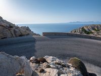 an empty road running along a cliff overlooking the water and ocean with rocks in the foreground