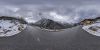 a panoramic view of an empty road and mountains in the distance, snow covered ground on either side