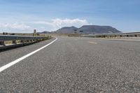 an empty roadway with hills and mountains in the background under a blue sky with clouds