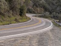 the road is winding by some trees and mountains, and is empty, while no cars go on it