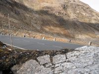 an empty road near rocky hillsides with a hill in the background, and a man on a bike riding down it