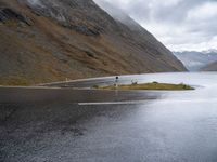 an empty paved road leads down to a lake with mountains in the background in the clouds