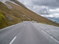 an empty road winds through the mountain with a sheep grazing along the roadway in front of it