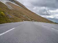 an empty road winds through the mountain with a sheep grazing along the roadway in front of it