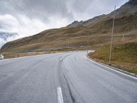 an empty road and a mountain with snow on top of it with clouds in the background