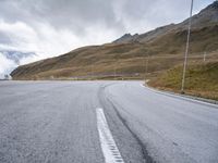 an empty road and a mountain with snow on top of it with clouds in the background