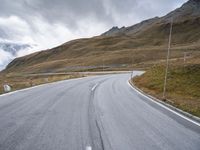 an empty road and a mountain with snow on top of it with clouds in the background