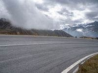 an empty road, a mountain and some clouds in the sky with fog over it