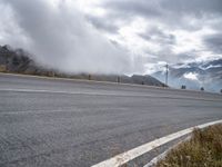 an empty road, a mountain and some clouds in the sky with fog over it