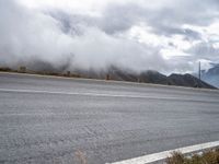 an empty road, a mountain and some clouds in the sky with fog over it