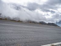 an empty road, a mountain and some clouds in the sky with fog over it