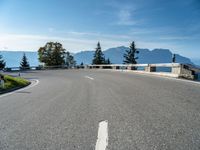 an empty road going along mountains with green bushes near by and a concrete barrier on either side