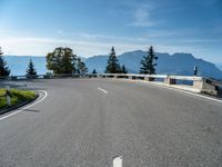 an empty road going along mountains with green bushes near by and a concrete barrier on either side