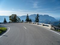 an empty road going along mountains with green bushes near by and a concrete barrier on either side