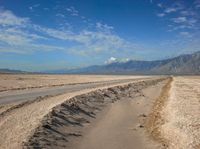 an empty road leads through a barren plain with mountains in the distance above a valley